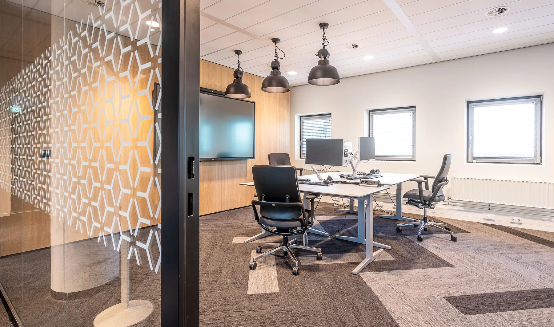 Bright commercial office with desks, glass partitions, and carpeted floors